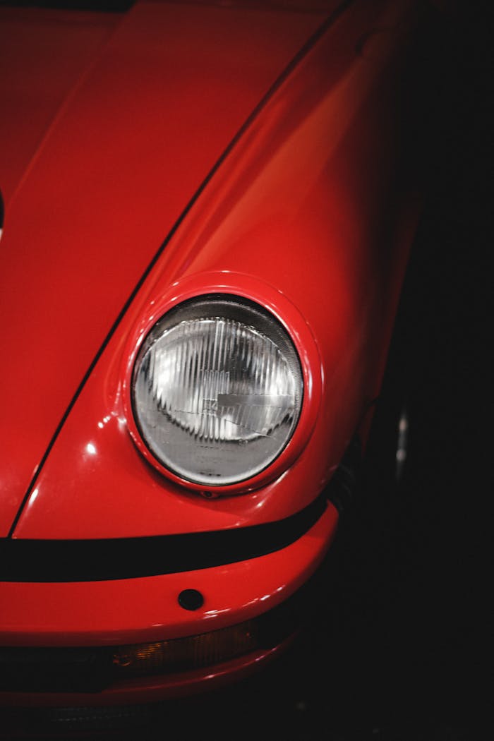 Detailed shot of a vintage red car's headlight, emphasizing its classic design.